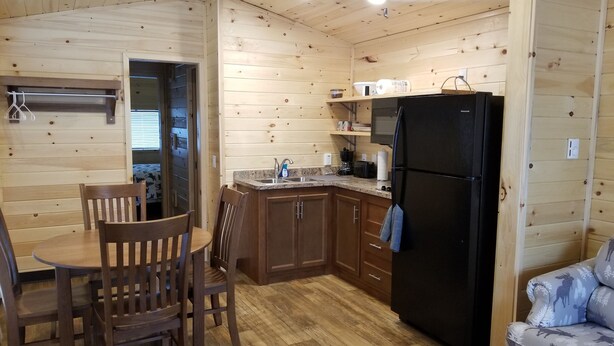 Una cocina compacta con armarios de madera, un refrigerador negro y una zona de comedor con sillas de madera.