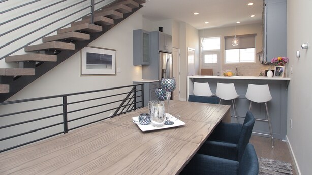 Une cuisine moderne dotée d’un îlot central, d’un coin repas avec une table en bois et d’un escalier avec une rampe en métal.