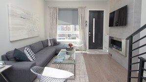 Un salon moderne avec un canapé gris, une table basse en verre et un téléviseur à écran plat fixé au mur.
