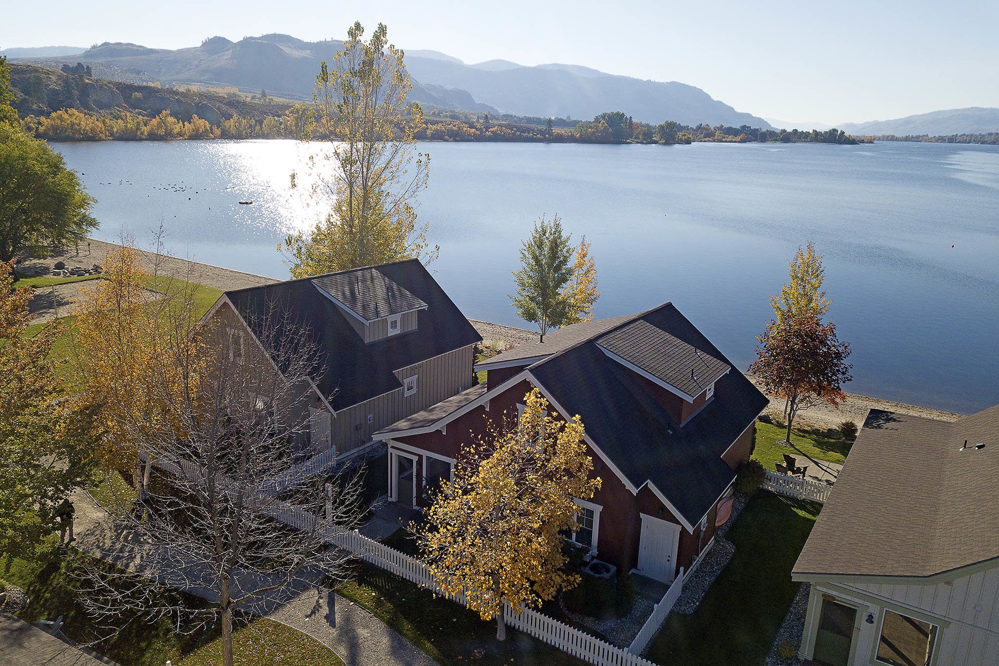 A residential area with houses near a lake, surrounded by trees and mountains in the background.