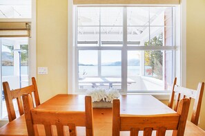 A dining area with a wooden table and chairs, a window with a view of the sea, and a white flower arrangement on the table. - Veranda Beach Cottages (Oroville)