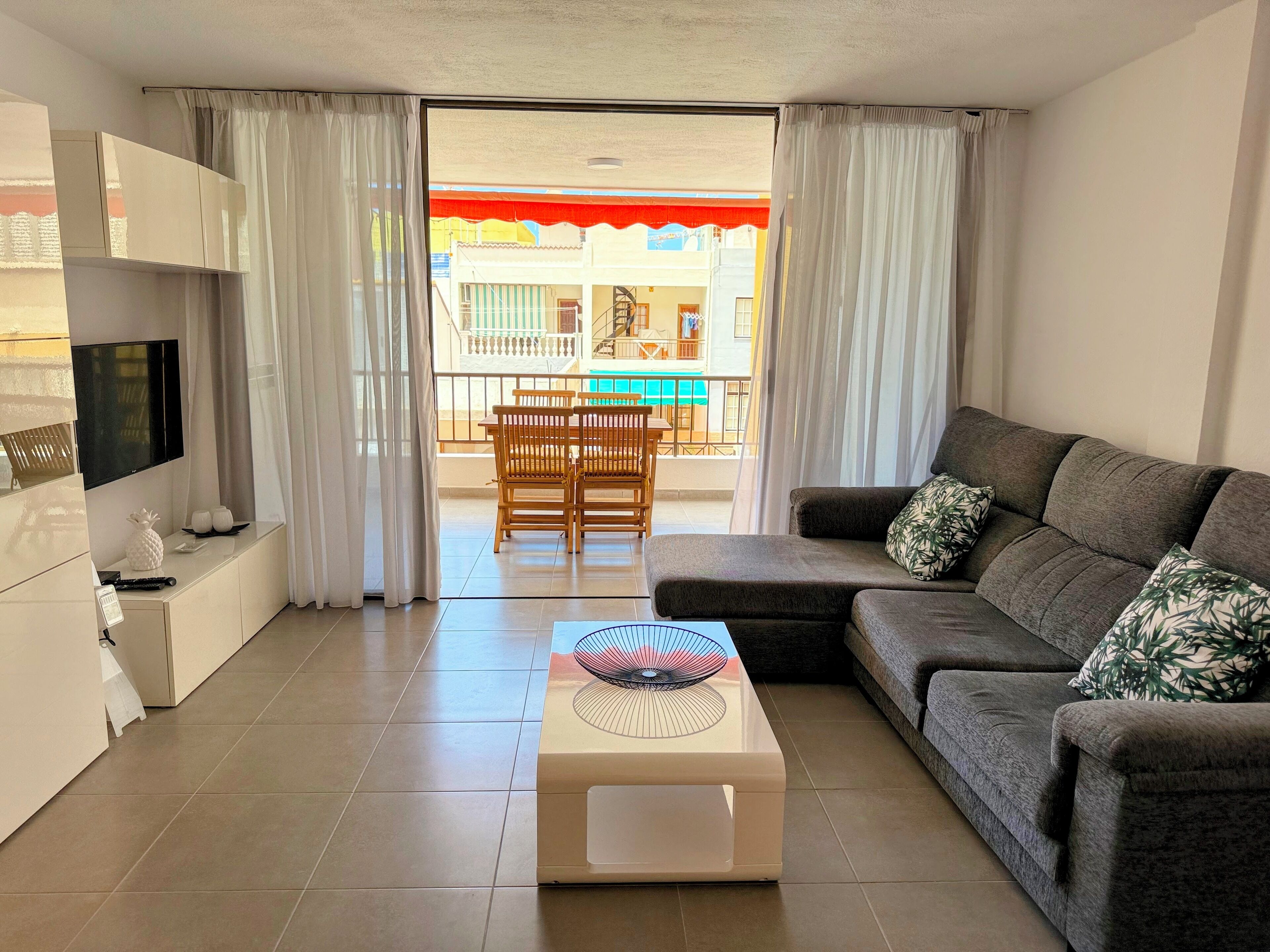 Een moderne woonkamer met een bank, een salontafel, een televisie en een balkon met uitzicht op een zwembad.