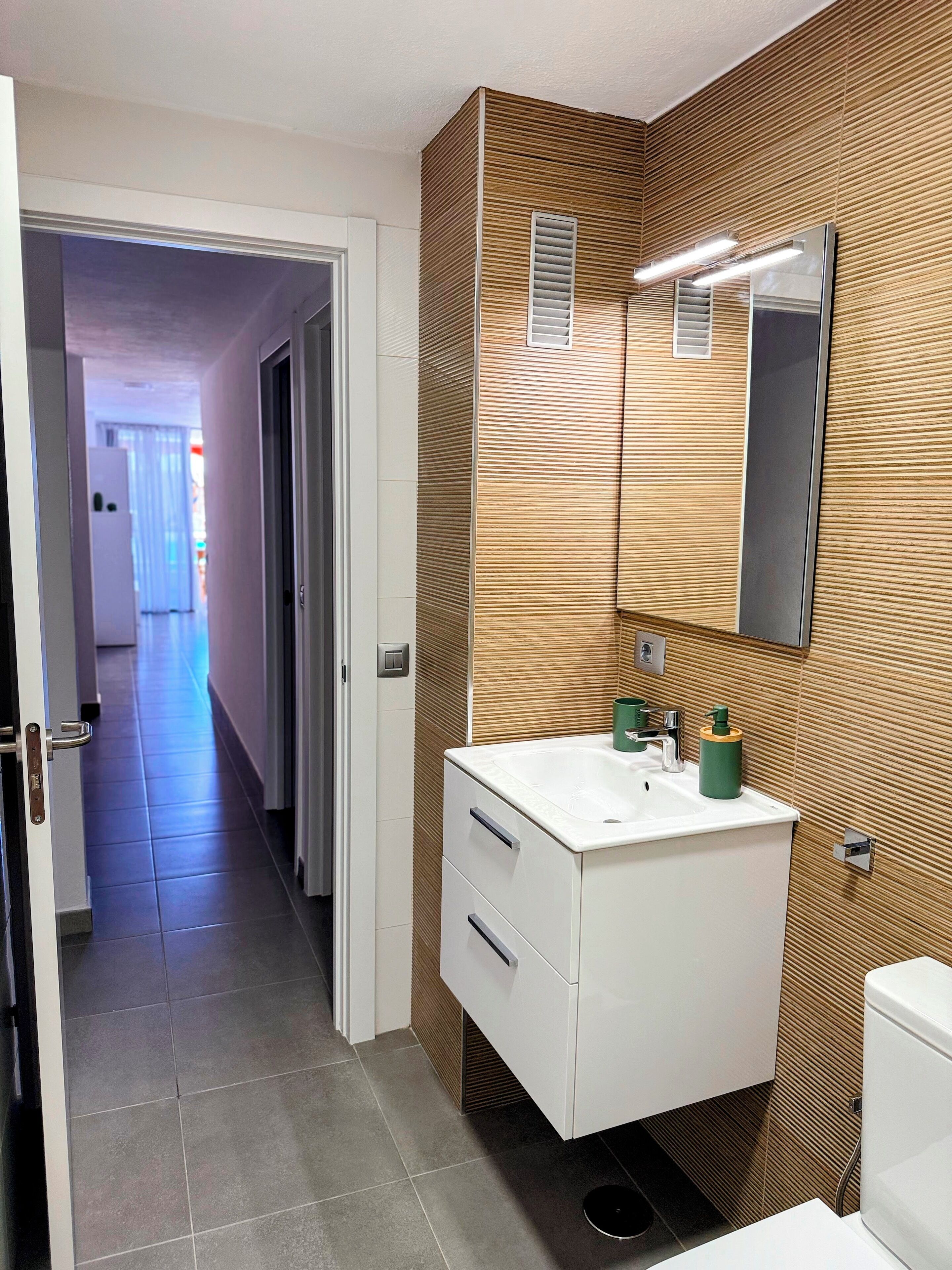 A modern bathroom with a wooden wall panel, a white sink, and a mirror.