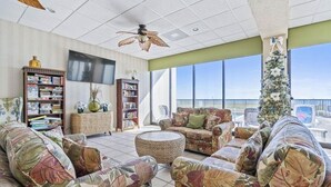 A spacious living room with a large window, a ceiling fan, and a Christmas tree. - Direct Oceanfront Condo Renovated & New Furniture-Pools,Hot Tub, Sauna,Free wifi (Myrtle Beach)