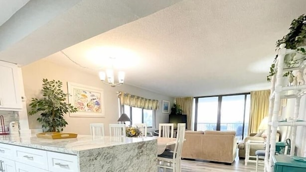 A modern kitchen with a marble island, white cabinetry, and a dining area with a high chair. - Direct Oceanfront Condo Renovated & New Furniture-Pools,Hot Tub, Sauna,Free wifi (Myrtle Beach)
