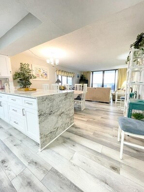 Une cuisine moderne dotée d’un îlot en marbre, de meubles blancs et d’un coin repas avec une chaise haute.