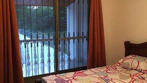 A bedroom with a bed, wooden headboard, curtains, and a view through a window with metal bars. - Villa Ensueño - House with Pool & Hot Tub (Flandes)