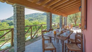 Ein überdachter Essbereich im Freien mit Tisch für vier Personen, Steinpfeilern und Blick auf eine gebirgige Landschaft.