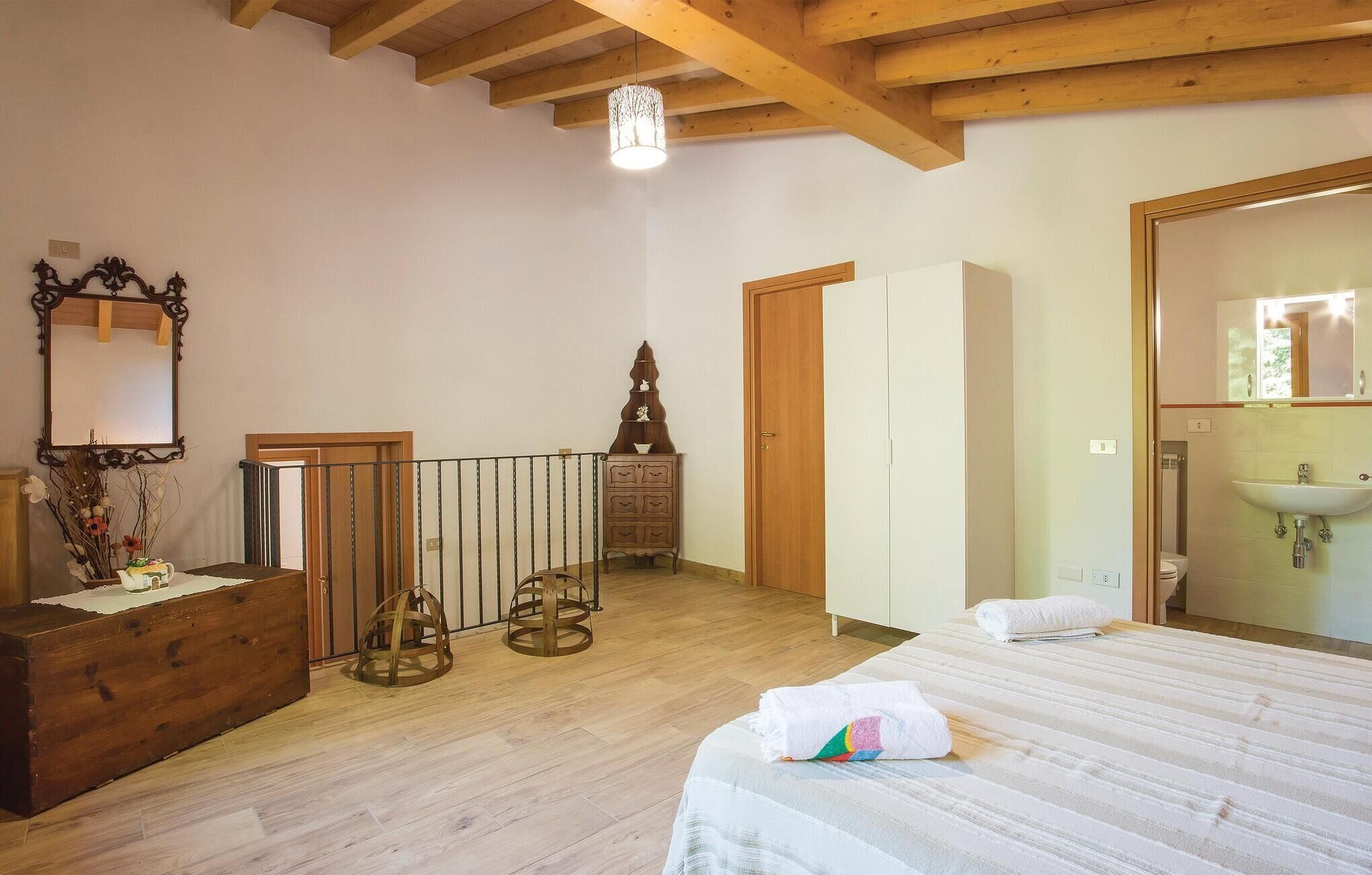 Une chambre avec un plancher en bois, un lit recouvert d’une couvre-lit à rayures, une commode, un miroir et une armoire.