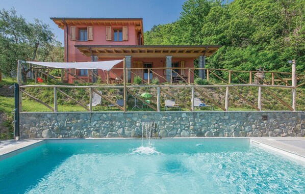 A swimming pool with a stone wall, a wooden deck, and a red building with windows in the background.