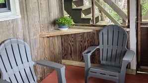 A porch with two Adirondack chairs, a window with a view of a wooden staircase, and a small potted plant on the windowsill. -  Oceanfront Classic Cottage (Salvo)