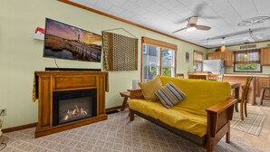 A living room with a fireplace, sofa, television, and kitchen area. -  Oceanfront Classic Cottage (Salvo)