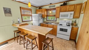 A kitchen with wooden cabinets, a large island with stools, a refrigerator, a microwave, and a stove. -  Oceanfront Classic Cottage (Salvo)