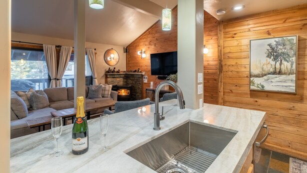 A modern kitchen with a marble countertop, stainless steel sink, and pendant lighting.