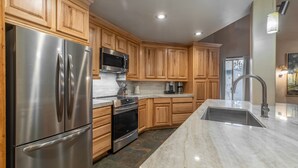 A modern kitchen with wooden cabinets, stainless steel appliances, and a marble countertop.