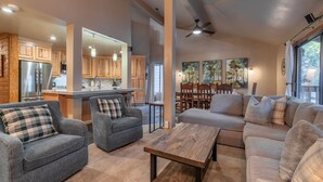 A spacious living area with a gray sofa, a wooden coffee table, and a kitchen area with wooden cabinets and a refrigerator.