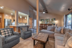 A spacious living area with a gray sofa, a wooden coffee table, and a kitchen area with wooden cabinets and a refrigerator.