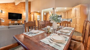 A dining area with a wooden table set for four, a television mounted on the wall, and wooden cabinets in the background.