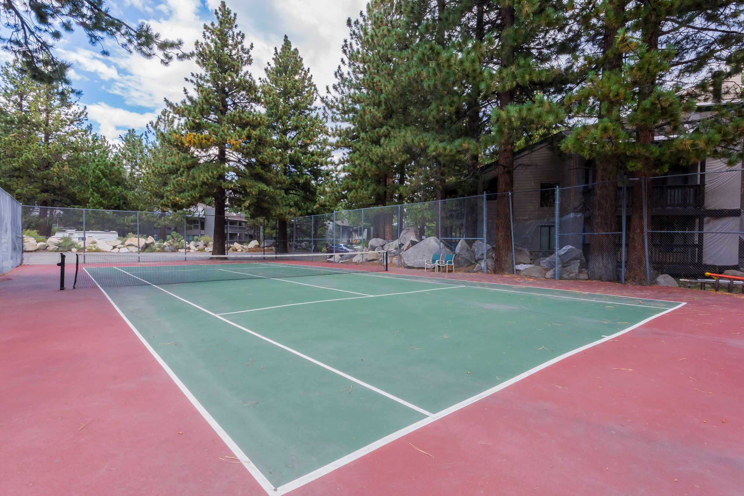 A tennis court with a net, surrounded by trees and a fence.