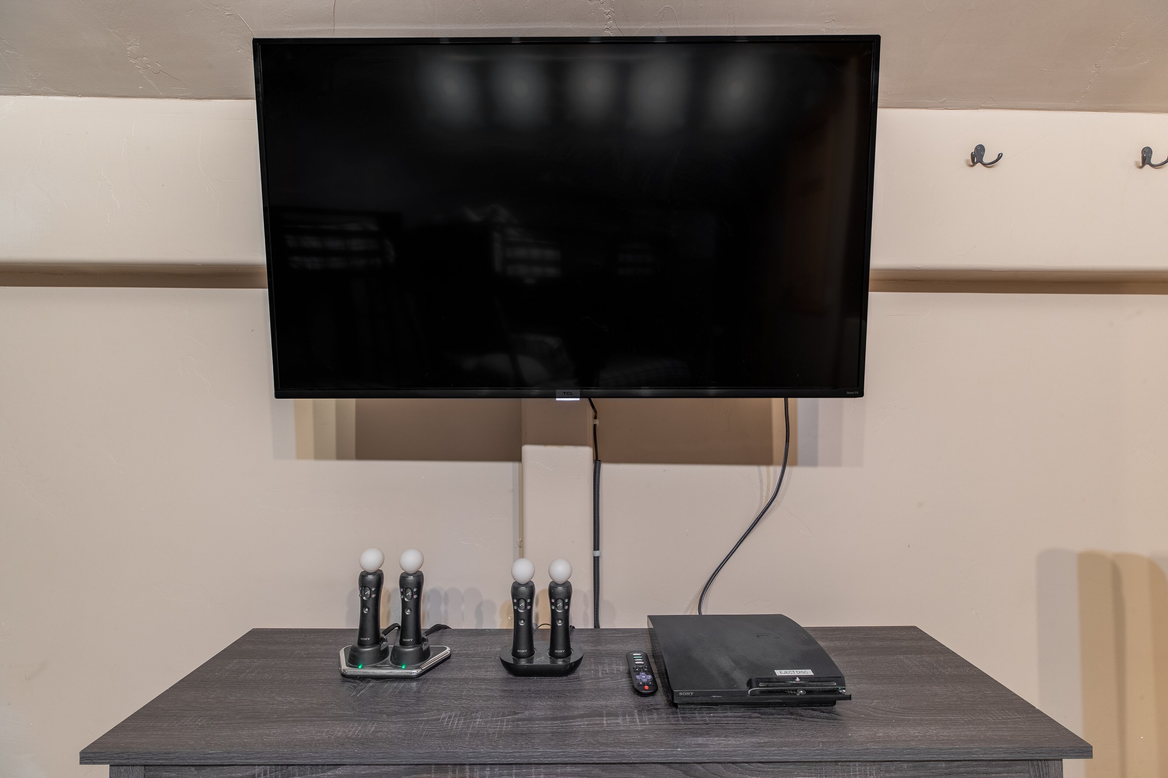 Ein Flachbildfernseher an der Wand, eine Spielkonsole und eine Fernbedienung auf einem Holztisch.