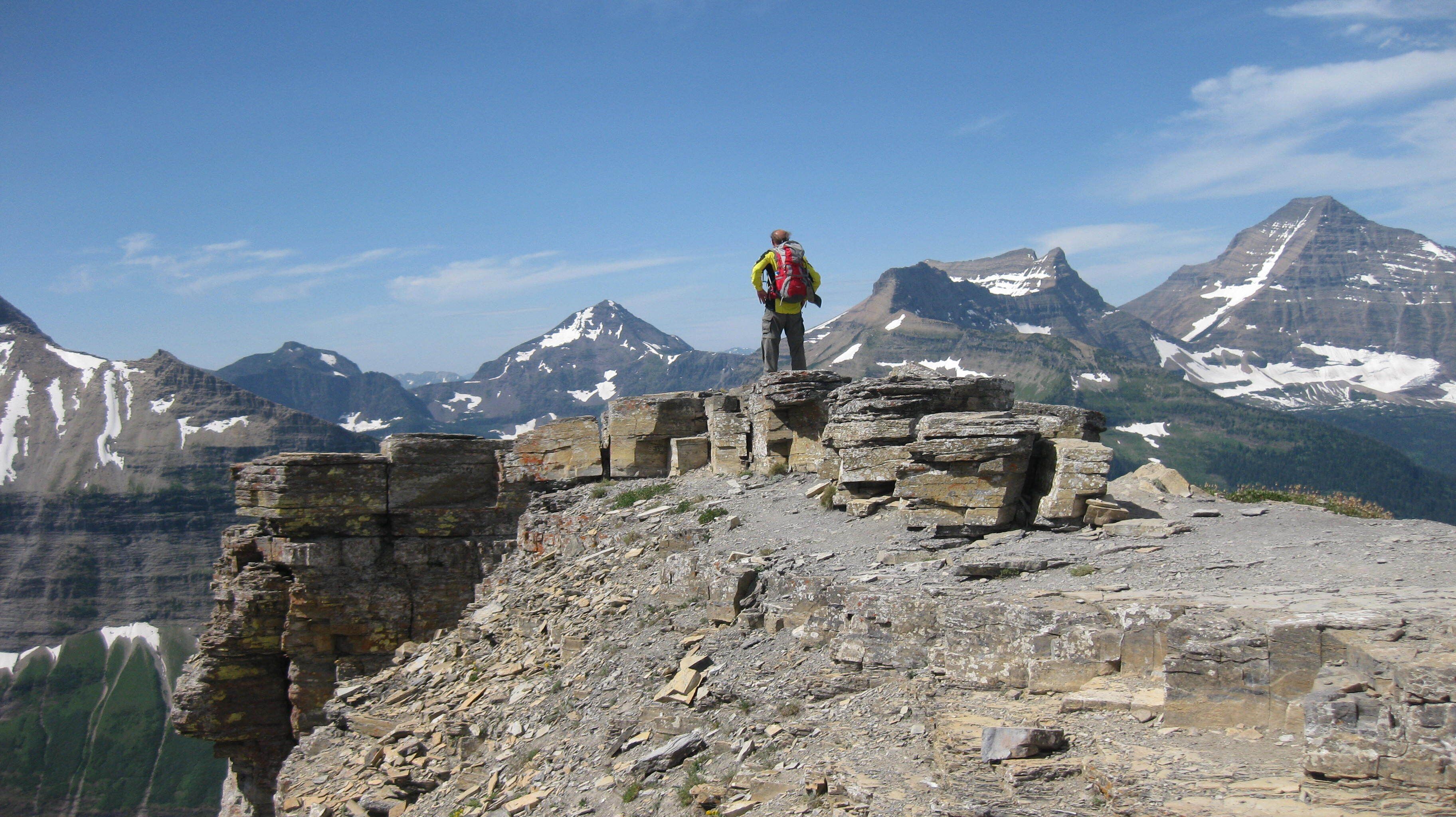 Eine Person steht auf einer felsigen Klippe mit einer Berglandschaft im Hintergrund.