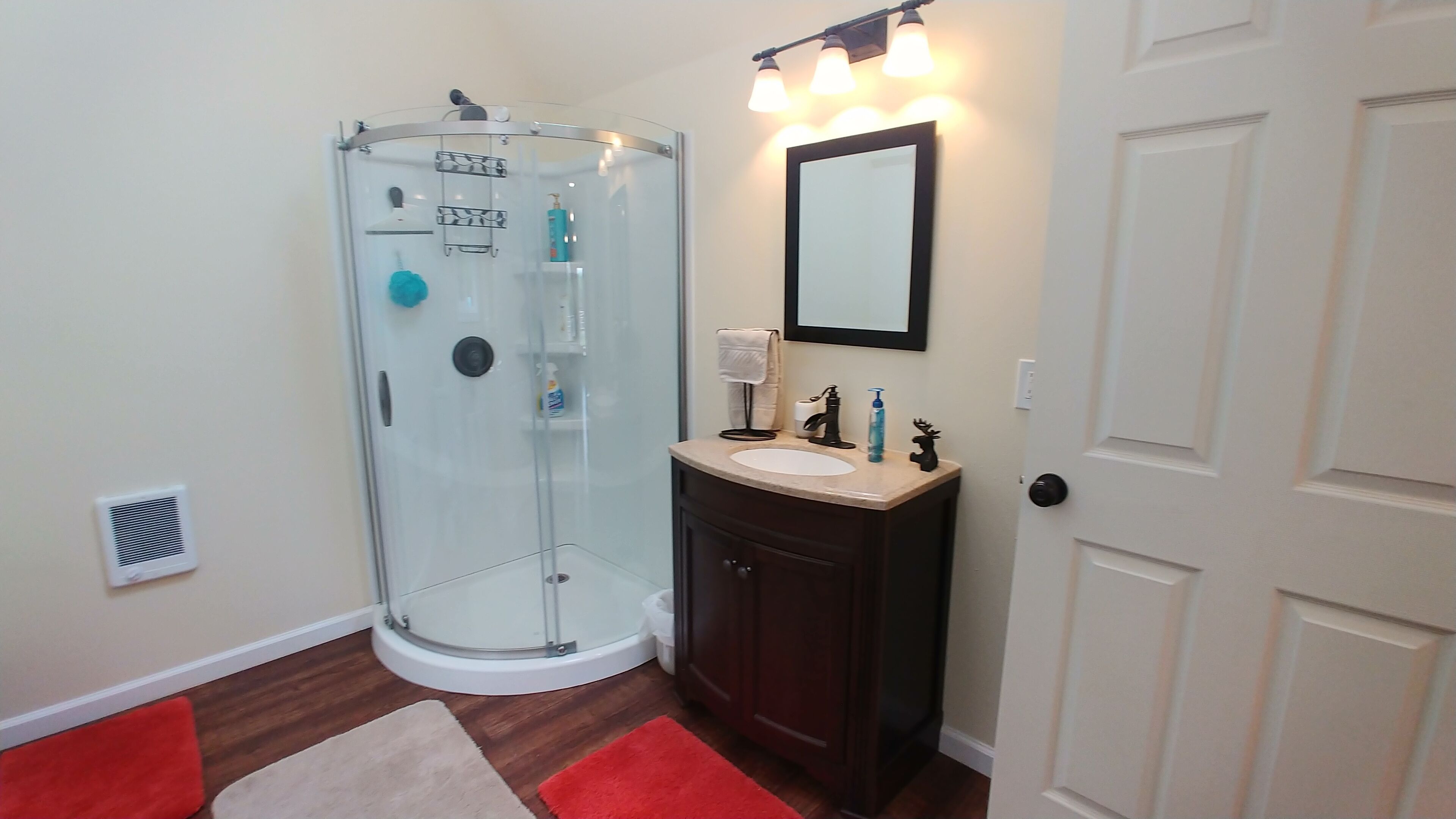 Un baño con cabina de ducha de vidrio, tocador con lavamanos y espejo.