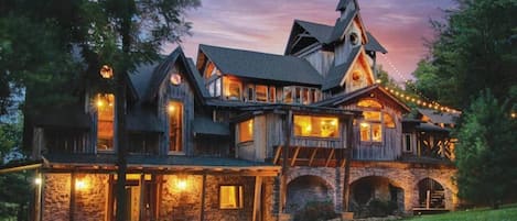 Una casa grande de madera de varios pisos, con zócalo de piedra, varios balcones y luces colgantes.