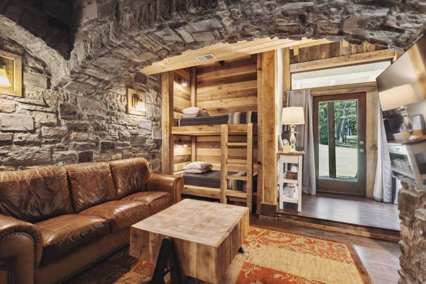 Ein rustikales Interieur mit Steinwand, Holzmöbeln und Blick durch eine Glastür.