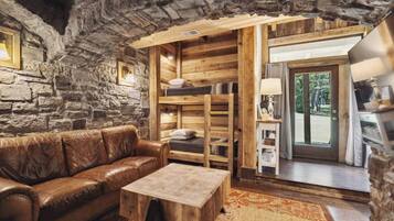 Ein rustikales Interieur mit Steinwand, Holzmöbeln und Blick durch eine Glastür.