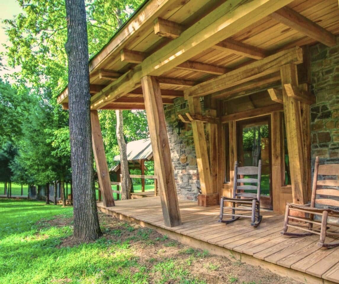 A wooden cabin with a porch, stone walls, and two rocking chairs.