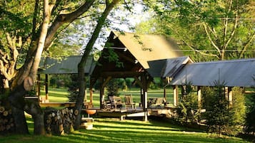 Ein rustikales Holz-Pavillon mit einem Reetdach, umgeben von einem gepflegten Rasen und Bäumen.