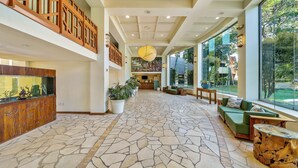 A spacious lobby with a stone floor, wooden furniture, and large windows offering a view of the outdoors. - Spacious Penthouse Studio w Ocean View Pool - Kaanapali Shores 942 (Lahaina)