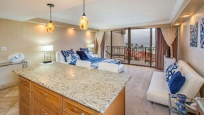 A spacious living area with a kitchen island, a balcony with a view, and a large window. - Spacious Penthouse Studio w Ocean View Pool - Kaanapali Shores 942 (Lahaina)