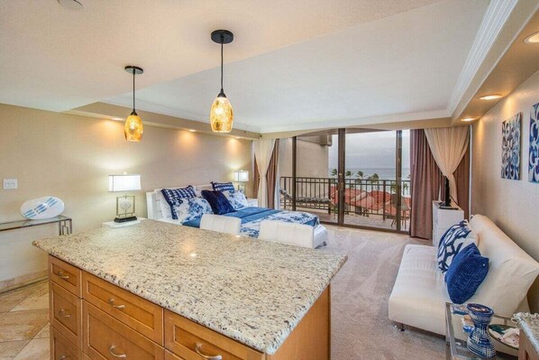 A spacious living area with a kitchen island, a balcony with a view, and a large window.