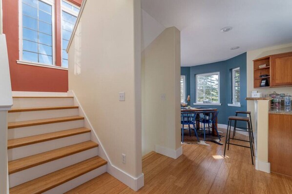 A spacious kitchen with a dining area, wooden stairs, and a view of the outdoors.