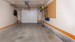 A parking garage with a concrete floor, a closed garage door, and a wall-mounted blue fire extinguisher. - Après Chalet – Luxury Town Home off Ski Hill Rd (Driggs)