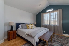 A bedroom with a bed, bedside tables, a bench, a window with curtains, and a patterned rug.