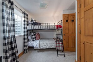 A bunk bed room with a window, curtains, and a door.