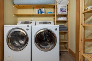 A laundry room with two front-loading washing machines and shelves above containing laundry supplies.