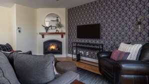 A living room with a fireplace, a mounted TV, and patterned wallpaper. - Après Chalet – Luxury Town Home off Ski Hill Rd (Driggs)