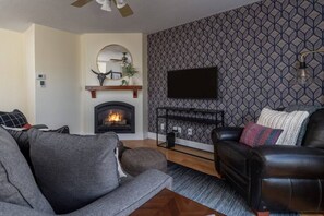 Een woonkamer met een open haard, een bevestigde televisie en behang met een patroon.