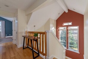 A spacious room with a wooden staircase, a view of a forest through a large window, and a small table with a plant.