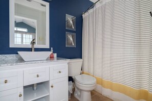 Une salle de bain avec un lavabo blanc, un miroir, des toilettes et un rideau de douche à rayures.