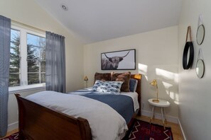 Une chambre à coucher avec un lit, une fenêtre, un tableau encadré, une table de chevet et un tapis.