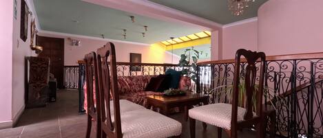 A dining area with wooden chairs and a table, a staircase with a wrought iron railing, and a chandelier.