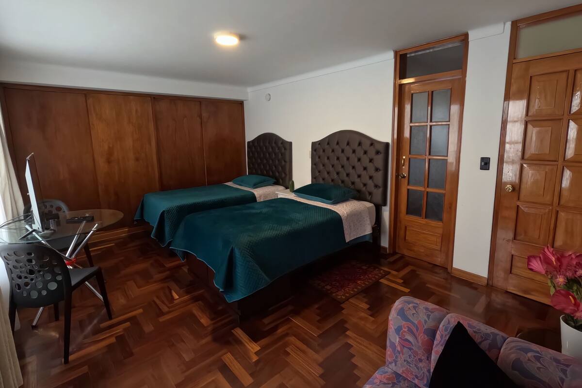Un dormitorio con dos camas, un armario de madera, un escritorio con silla y una puerta de madera con paneles de vidrio.