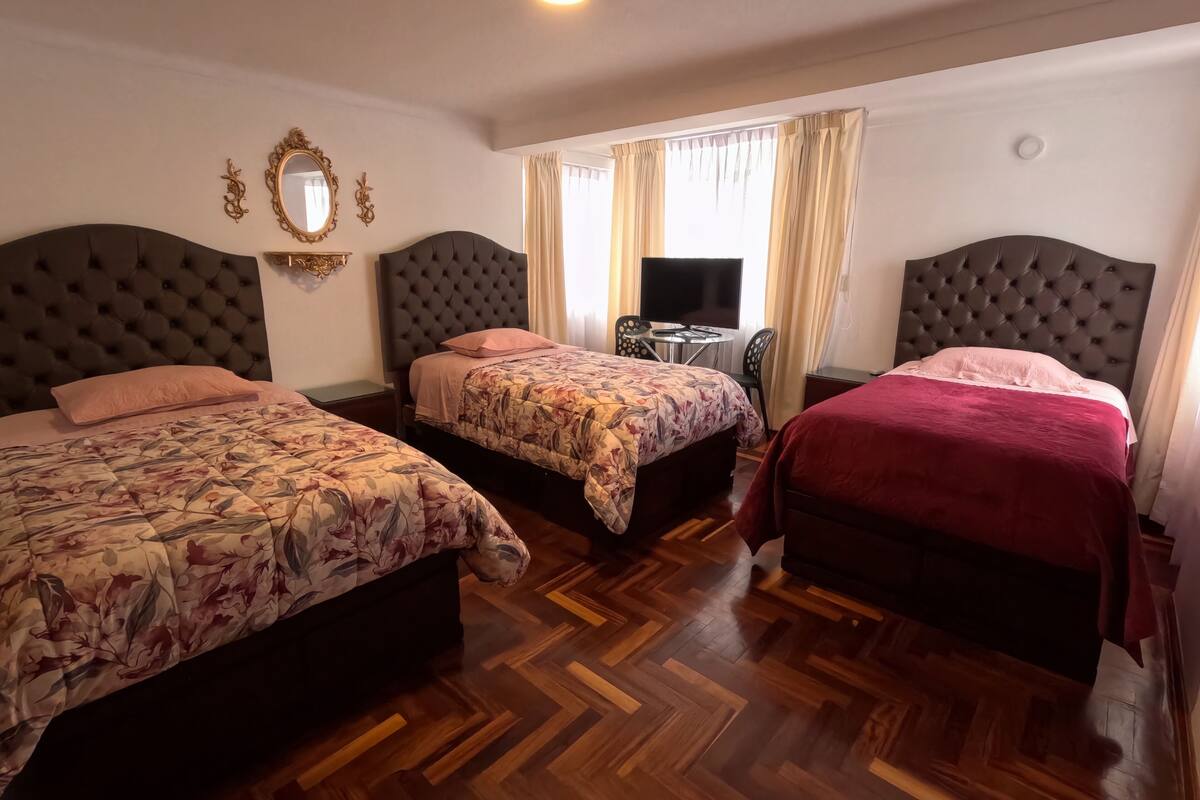 Una habitación de hotel con tres camas, un televisor y un escritorio.