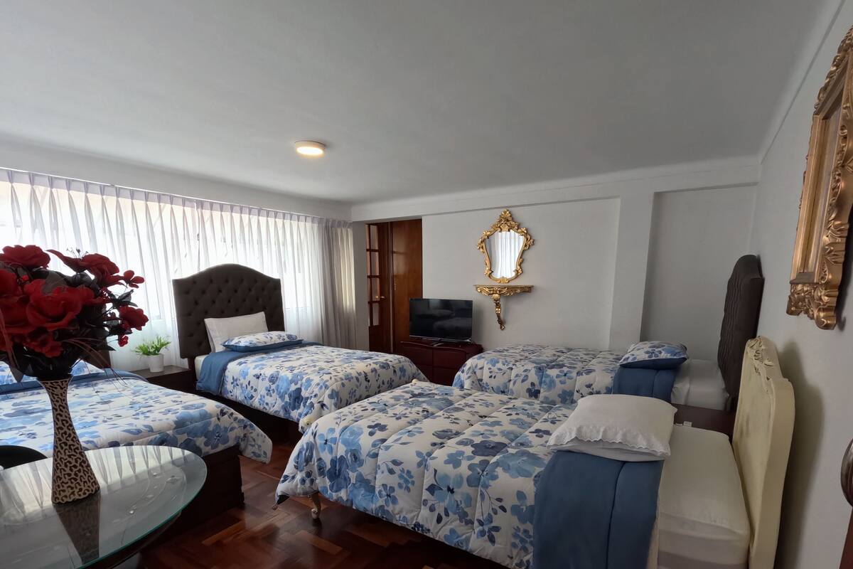 Una habitación de hotel con dos camas, una mesa de comedor, un televisor y un espejo.