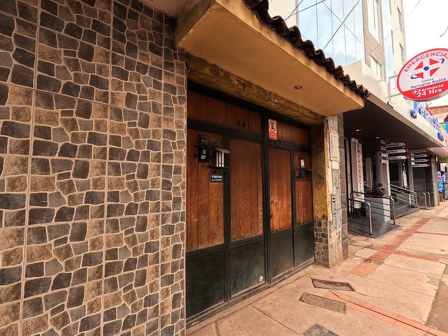 A building with a stone facade and a wooden door. There is a sign indicating a pharmacy and a 24-hour emergency service.