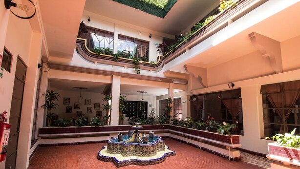 Ein geräumiges Atrium mit einer zentralen Fontäne, mehreren Ebenen mit Balkonen und zahlreichen Zimmerpflanzen.
